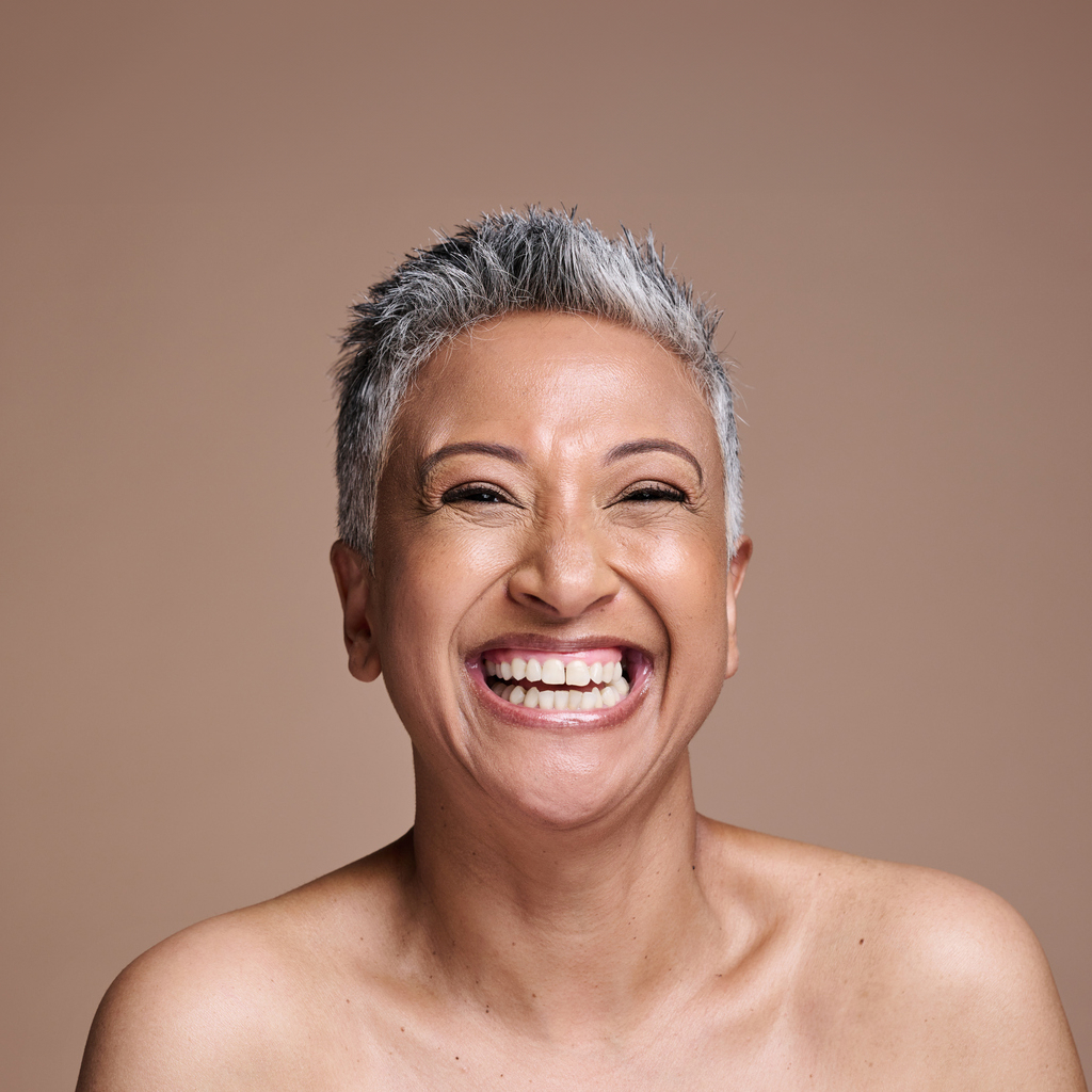 women with caramel skin and short grey hair, smiling against a brown background