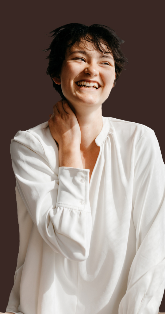 person wearing a long white button down on a brown background smiling