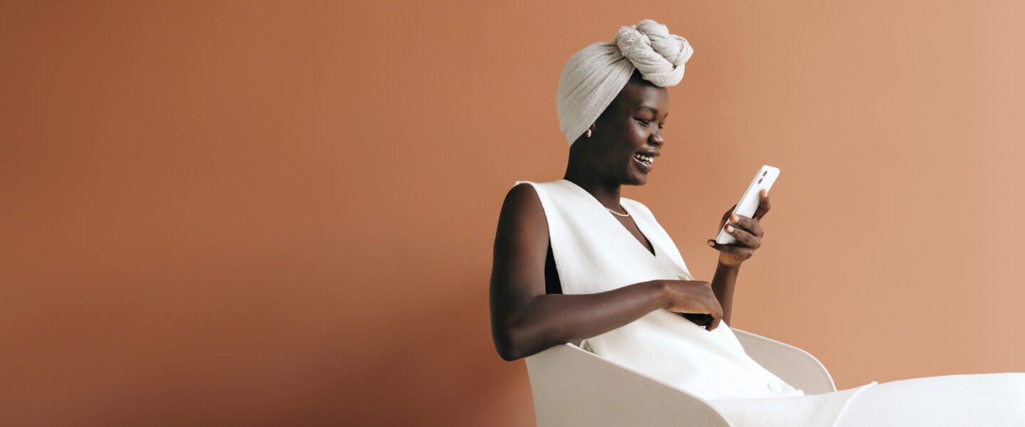 women dressed in white looking down at cellphone happily on a brown background