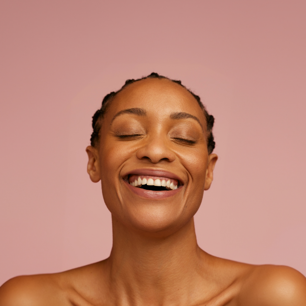 women smiling on a blush background with eyes closed