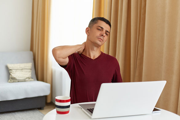 Man bothered by neck discomfort while working on laptop
